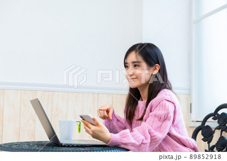 パソコンで調べながら慎重にアプリでネットショッピングをする若い女性 89852918