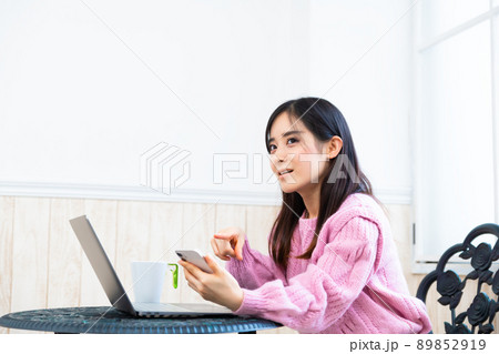 パソコンで調べながら慎重にアプリでネットショッピングをする若い女性 89852919