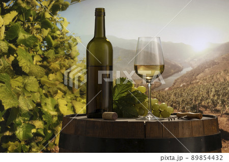 Design for card, magazine or brochure cover. White wine glass and bottle on wooden barrel over nature landscape background. Winemaking and festivals concept 89854432