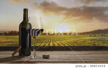 Charm. Still life with red wine glass and bottle on wooden table over background of panoramic view of lush vineyards at sunset. Tasting, festivals concept 89854459