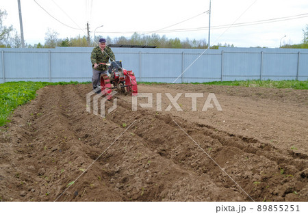 A man cultivates a field with a walk-behind tractor. A man cultivates a field with a walk-behind tractor. 89855251