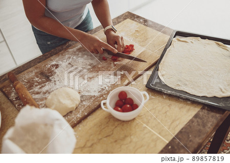 A housewife in the kitchen cuts tomatoes on a wooden board for pizza preparing for baking A housewife in the kitchen cuts tomatoes on a wooden board for pizza preparing for baking 89857819