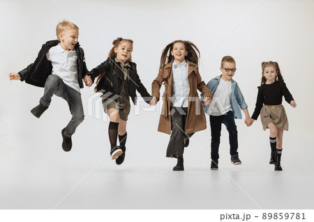 Happy school and preschool age children, girls and boys running, jumping isolated on grey studio background. Beauty, kids fashion, education, happy childhood concept. Happy school and preschool age children, girls and boys running, jumping isolated on grey studio background. Beauty, kids fashion, education, happy childhood concept. 89859781