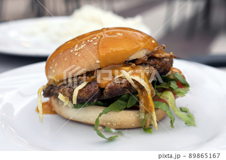 fresh delicious mouth-watering hamburger with cutlet, salad and fried onions and mustard on a plate in a summer restaurant in the evening outdoor on the street veranda close-up. minimalistic lifestyle fresh delicious mouth-watering hamburger with cutlet, salad and fried onions and mustard on a plate in a summer restaurant in the evening outdoor on the street veranda close-up. minimalistic lifestyle 89865167