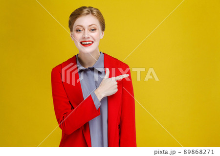 Redhead business woman in red suit showing at copy space. Studio shot, isolated on yellow background 89868271