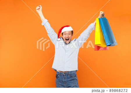 Excited man hands up, holding packets, scream or shout and looking at camera with big eyes and open mouth. Studio shot, orange wall Excited man hands up, holding packets, scream or shout and looking at camera with big eyes and open mouth. Studio shot, orange wall 89868272