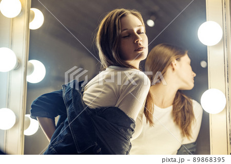 Beautiful sexy girl near the mirror in the dressing room in a jeans jacket. Indoor shot 89868395