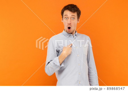Shocked man looking at camera and pointing finger himself. Studio shot, orange background Shocked man looking at camera and pointing finger himself. Studio shot, orange background 89868547
