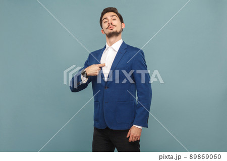 Proud man pointing finger himself. portrait of handsome bearded businessman in blue suit and white shirt, with smart watch. Indoor studio shot, isolated on light blue background Proud man pointing finger himself. portrait of handsome bearded businessman in blue suit and white shirt, with smart watch. Indoor studio shot, isolated on light blue background 89869060