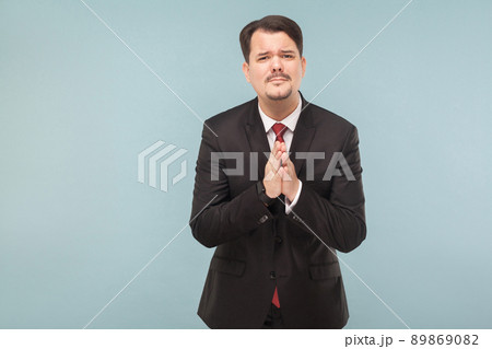 I was detained at work and asked my wife to forgive. indoor studio shot. isolated on light blue background. handsome businessman with black suit, red tie and mustache looking at camera. 89869082