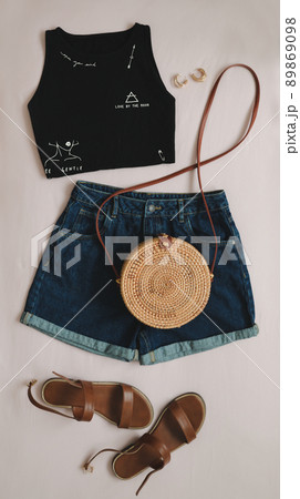 flat lay composition with female top, denim shorts, sandals and a wicker rattan bag on beige background top view 89869098