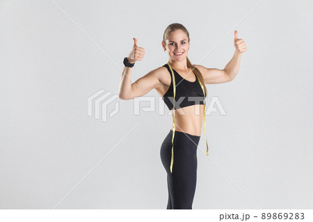 Closeup powerful muscular girl, showing thumbs up at camera and smiling. Studio shot, gray background 89869283
