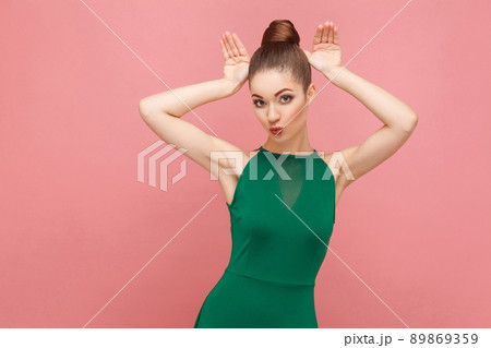 Cute woman showing rabbit ears. Expression emotion and feelings concept. Studio shot, isolated on pink background Cute woman showing rabbit ears. Expression emotion and feelings concept. Studio shot, isolated on pink background 89869359