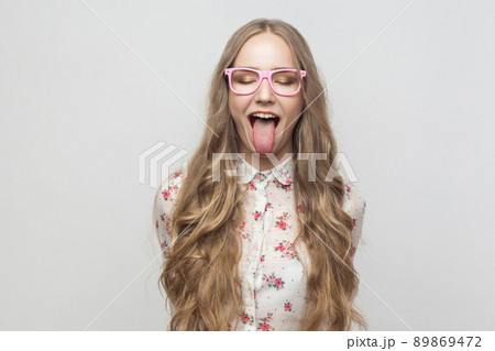 Happy and crazy concept. Teenager girl closed eyes and showing tongue at camera. Studio shot, isolated on gray background 89869472