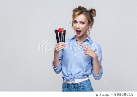 Beautiful blonde girl, holding and pointing finger to many pofessional brush, looking at camera. Isolated on gray background 89869619