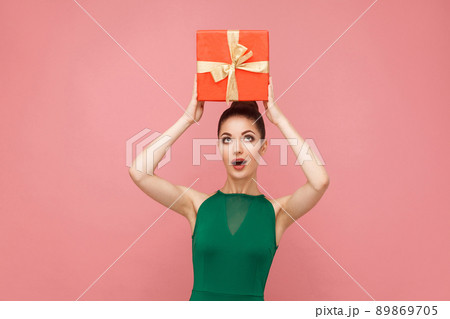 Woman holding red gift box on head. Expression emotion and feelings concept. Studio shot, isolated on pink background 89869705