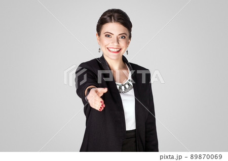 Woman in suit looking at camera and showing handshake sign. Studio shot, indoor. Isolated on grey background Woman in suit looking at camera and showing handshake sign. Studio shot, indoor. Isolated on grey background 89870069