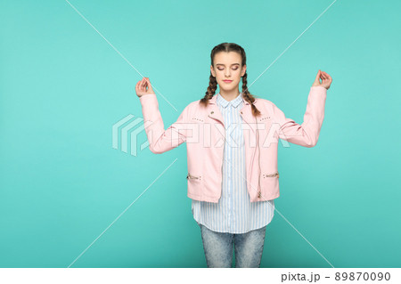 meditation and yoga portrait of beautiful cute girl standing with makeup and brown pigtail hairstyle in striped light blue shirt pink jacket. indoor, studio shot isolated on blue or green background. 89870090