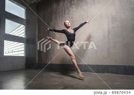 Beautiful graceful ballerine in black practice ballet positions near large window in light hall. Ballet class training. Studio shot, gray background 89870434