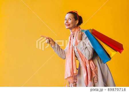 Happiness young adult woman pointing finger on copy space and looking at camera and toothy smile. On yellow background. Isolated shot Happiness young adult woman pointing finger on copy space and looking at camera and toothy smile. On yellow background. Isolated shot 89870718