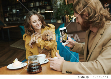 Portrait of serious modern guy with beard sitting at round table in loft cafe and calling by mobile phone Portrait of serious modern guy with beard sitting at round table in loft cafe and calling by mobile phone 89870771