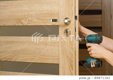 handyman repair the door lock in the room. man repairing the door handle furniture. carpenter at lock installation with electric drill into interior wood door handyman repair the door lock in the room. man repairing the door handle furniture. carpenter at lock installation with electric drill into interior wood door 89871162