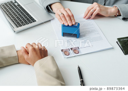 Medium close-up shot of unrecognizable consular officer putting approval seal on visa application form for Muslim woman after interview 89873364