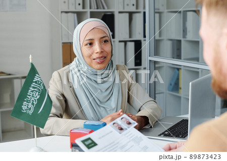 Modern Muslim woman wearing hijab working as consular officer in Saudi Arabia embassy interviewing Caucasian man for visitor visa 89873423