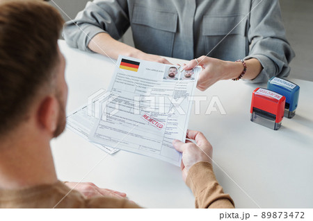 High angle view of unrecognizable consular officer returning visa application form paper with rejected stamp on it to applicant High angle view of unrecognizable consular officer returning visa application form paper with rejected stamp on it to applicant 89873472