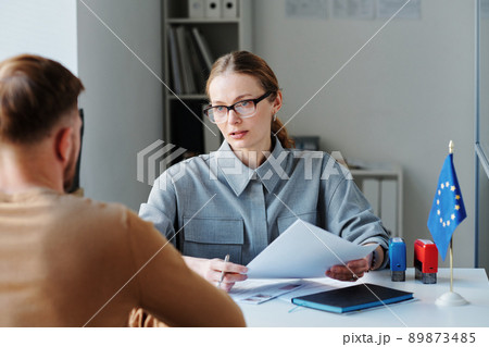 Mature woman working as consular officer in embassy interviewing unrecognizable man sitting in front of her for schengen visa 89873485