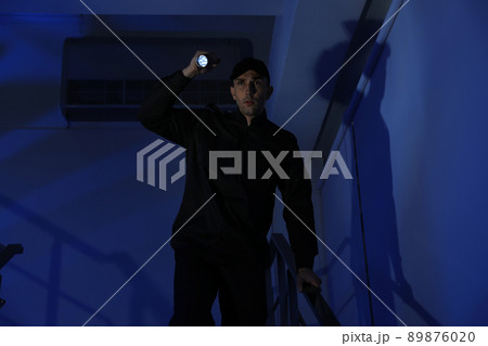 Male security guard with flashlight on stairs in darkness Male security guard with flashlight on stairs in darkness 89876020