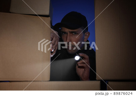 Security guard with flashlight looking through pile of cardboard boxes in dark room Security guard with flashlight looking through pile of cardboard boxes in dark room 89876024