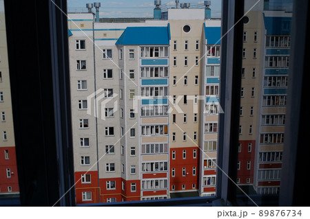View of a multi-storey panel residential building in the Russian province from the window of a neighboring house. View of a multi-storey panel residential building in the Russian province from the window of a neighboring house. 89876734