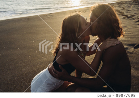 Against the background of sand and ocean in the sun in the sun, a woman in shorts kisses a man 89877698