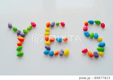 The inscription YES, inlaid with multicolored dragees on a light, shiny surface. 89877823