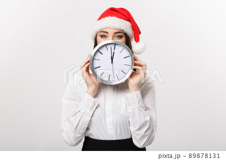 Time management concept - Young business woman with santa hat hiding behind a clock isolated over white background. Time management concept - Young business woman with santa hat hiding behind a clock isolated over white background. 89878131