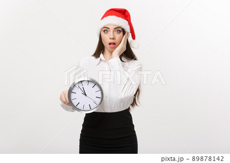 Time management concept - Young business woman with santa hat holding a clock isolated over white background. Time management concept - Young business woman with santa hat holding a clock isolated over white background. 89878142