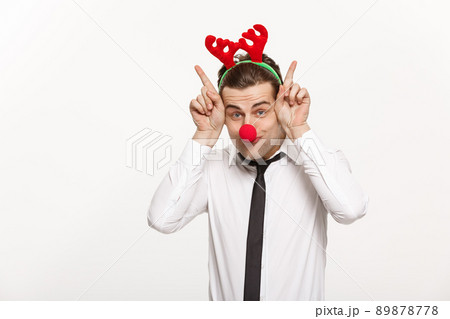 Christmas Concept - Handsome Business man wearing reindeer hairband making funny facial expression. 89878778