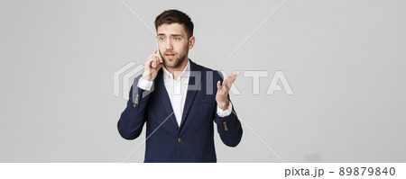 Business Concept - Portrait young handsome angry business man in suit talking on phone looking at camera. White background. Business Concept - Portrait young handsome angry business man in suit talking on phone looking at camera. White background. 89879840