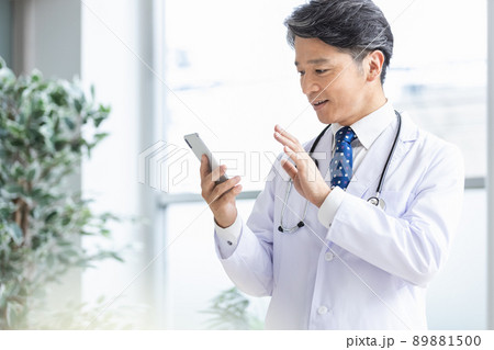 スマホを持って窓際に立つ白衣の医師 89881500