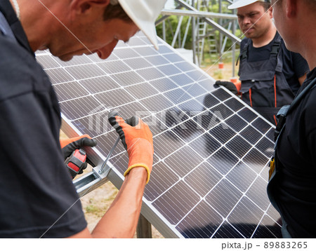Workers installing solar panel on metal beams. Close up image of men wearing workwear and helmets 89883265