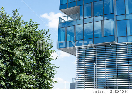 a building with mirrored windows next to a green tree, Against the background of a blue sky 89884030