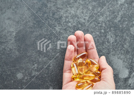 A person holds an omega-3 fatty acid capsule against a gray background. The concept of medicine and healthy living. Top view. 89885890