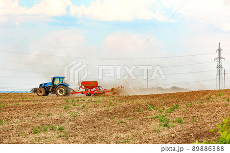 An agricultural tractor with a trailed seeder cultivates the soil in the field by applying the necessary fertilizers. 89886388