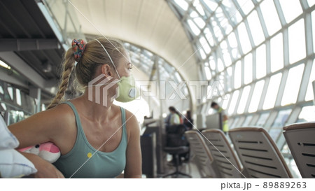 Woman caucasian at airport with wearing protective medical mask on head against the background of the plane. Coronavirus sars-cov-2 covid-19. 89889263