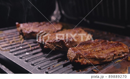 Delicious juicy meat steak cooking on grill. Prime beef fry on electric roaster, rosemary, black pepper, salt. Slow motion. Delicious juicy meat steak cooking on grill. Prime beef fry on electric roaster, rosemary, black pepper, salt. Slow motion. 89889270