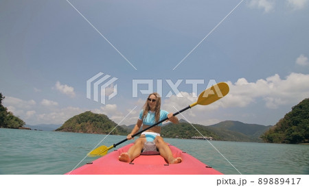 Sportive woman rows pink plastic canoe along sea water. Positive sports girl hand padding on kayak, front view. Sportive woman rows pink plastic canoe along sea water. Positive sports girl hand padding on kayak, front view. 89889417