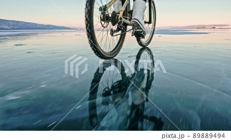 Woman is riding bicycle on the ice. Tires on bike are covered wi Woman is riding bicycle on the ice. Tires on bike are covered wi 89889494