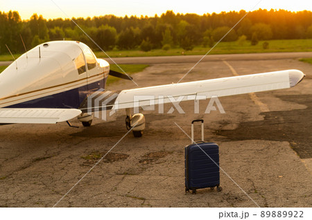 A blue suitcase and a parked small private jet. Quadruple plane with a propeller for an air taxi in the sunset. Self travel concept. plane for VIP persons. A blue suitcase and a parked small private jet. Quadruple plane with a propeller for an air taxi in the sunset. Self travel concept. plane for VIP persons. 89889922