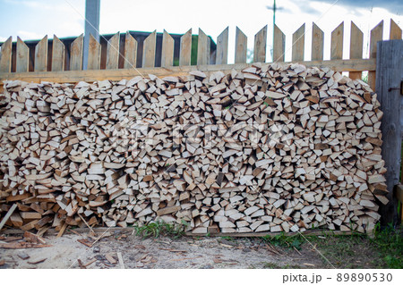 Firewood is stacked in a woodpile along the fence against the blue sky Firewood is stacked in a woodpile along the fence against the blue sky 89890530